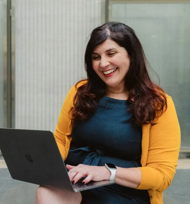 Happy woman in yellow cardigan on her laptop